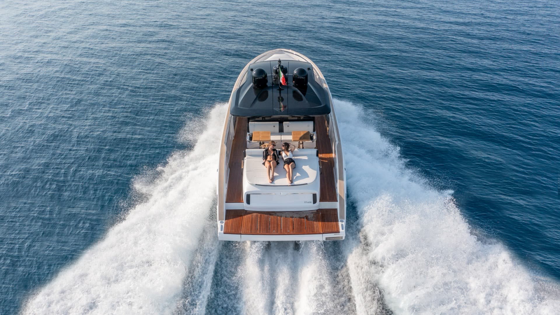 Aerial view of an Invictus TT420 underway on open water with two guests relaxing on the stern sun pad
